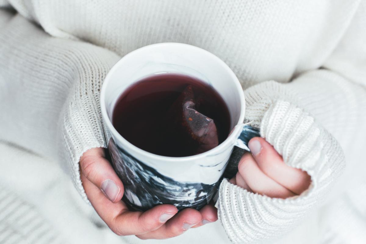 Woman in a warm white sweater holds a mug of hot tea